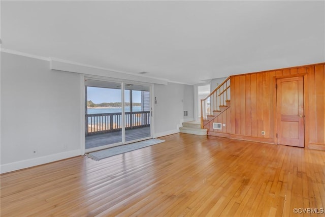 unfurnished living room featuring stairs, light wood-style floors, baseboards, and ornamental molding