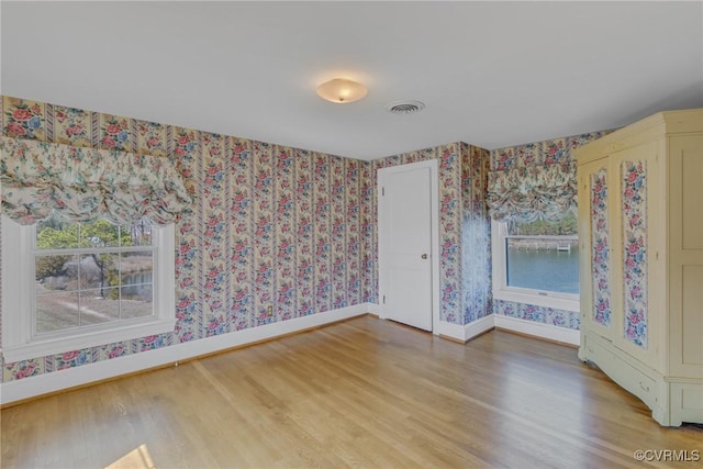 spare room featuring wallpapered walls, visible vents, baseboards, and light wood finished floors