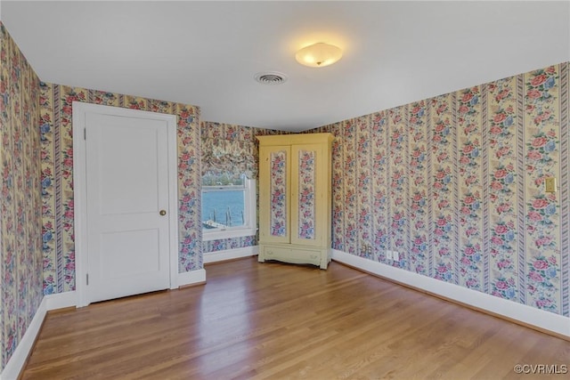 unfurnished room with visible vents, baseboards, wood finished floors, and wallpapered walls