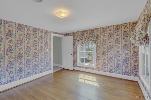 unfurnished room featuring wallpapered walls, wood finished floors, and baseboards