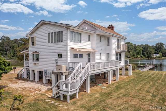 rear view of property featuring a lawn, a chimney, stairs, and a deck with water view