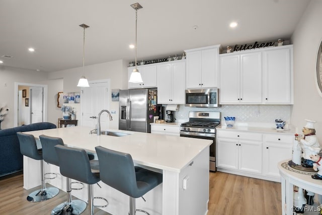 kitchen featuring decorative light fixtures, sink, backsplash, stainless steel appliances, and a center island with sink