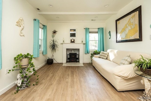 living room featuring light hardwood / wood-style floors, a wood stove, and beamed ceiling