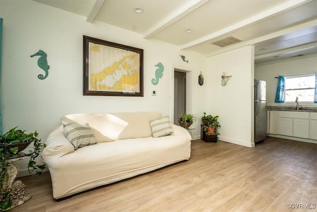 living room featuring sink, light hardwood / wood-style flooring, and beamed ceiling