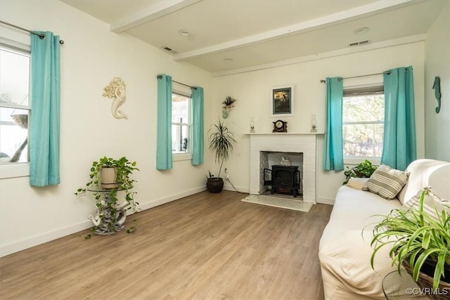 living room featuring a wealth of natural light, beam ceiling, wood-type flooring, and a wood stove