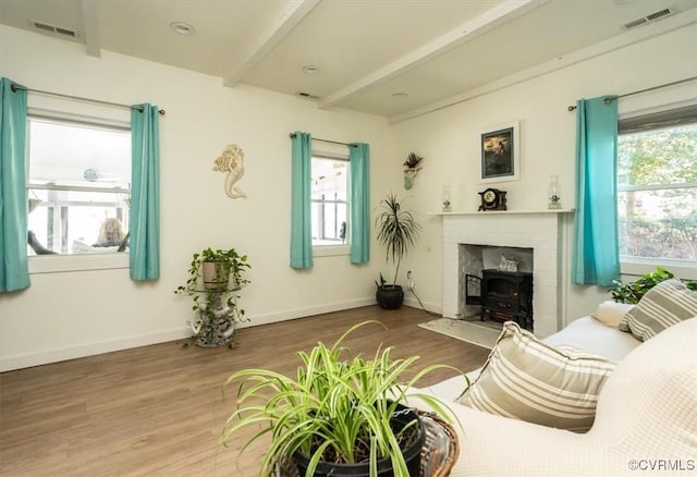 living room featuring wood-type flooring, a wood stove, and beamed ceiling