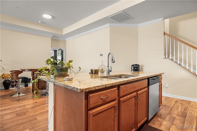 kitchen featuring stainless steel dishwasher, sink, light hardwood / wood-style flooring, light stone counters, and a center island with sink