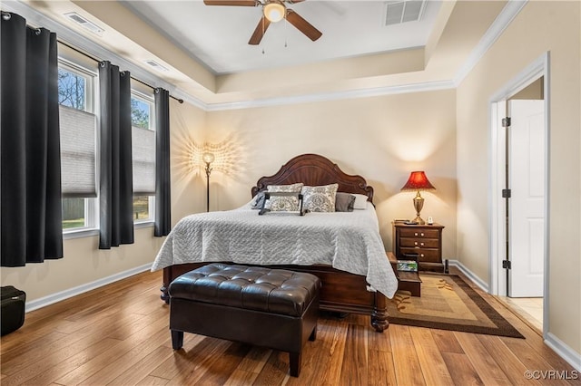 bedroom with ceiling fan, a raised ceiling, ornamental molding, and wood-type flooring