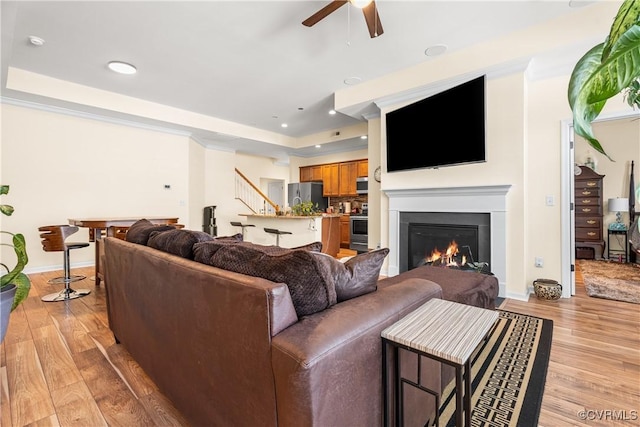 living room featuring ceiling fan, a raised ceiling, and light hardwood / wood-style floors