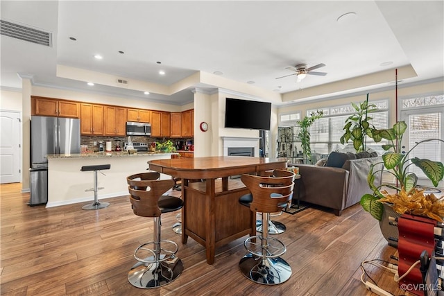 kitchen with a kitchen breakfast bar, a raised ceiling, light stone counters, dark hardwood / wood-style floors, and stainless steel appliances