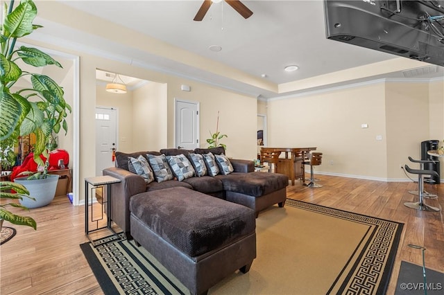 living room with light wood-type flooring, ceiling fan, crown molding, and a tray ceiling