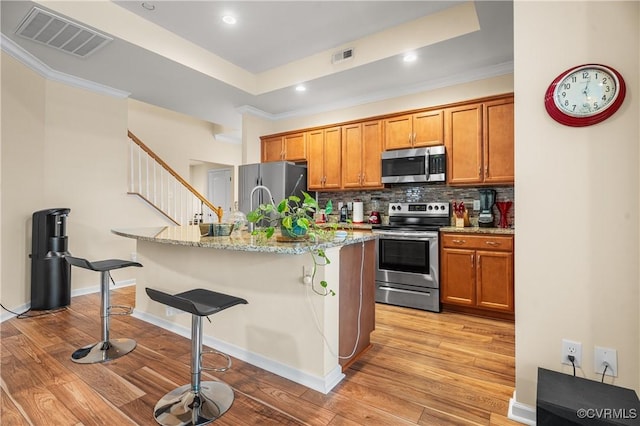 kitchen featuring stainless steel appliances, backsplash, light stone counters, a breakfast bar, and a center island with sink