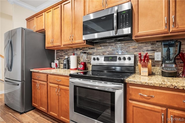 kitchen with crown molding, appliances with stainless steel finishes, backsplash, light stone counters, and light hardwood / wood-style floors