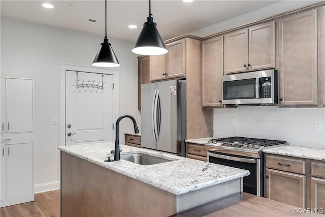 kitchen with sink, light stone counters, decorative light fixtures, a kitchen island with sink, and appliances with stainless steel finishes