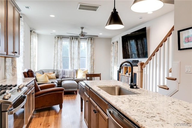 kitchen with light stone countertops, sink, stainless steel appliances, decorative light fixtures, and light wood-type flooring