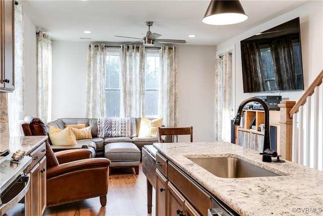 kitchen featuring light stone countertops, wood-type flooring, ceiling fan, and sink