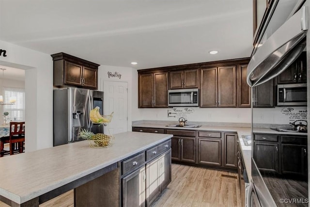 kitchen with dark brown cabinetry, a kitchen island, light wood-type flooring, and appliances with stainless steel finishes