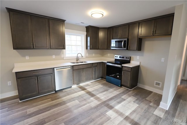 kitchen featuring appliances with stainless steel finishes, light hardwood / wood-style flooring, dark brown cabinets, and sink