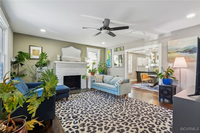 living room with ceiling fan, sink, wood-type flooring, and a fireplace