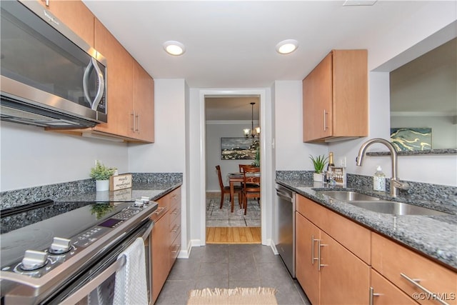 kitchen with dark tile patterned flooring, sink, dark stone countertops, ornamental molding, and appliances with stainless steel finishes