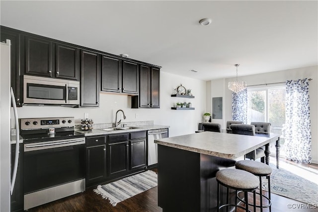 kitchen with sink, hanging light fixtures, appliances with stainless steel finishes, a kitchen breakfast bar, and a kitchen island