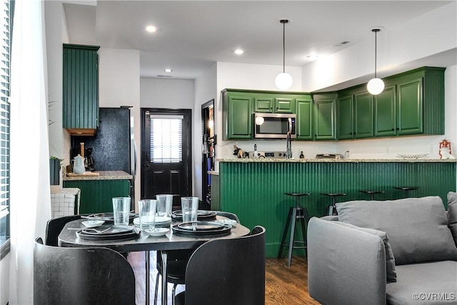 kitchen with green cabinets, dark hardwood / wood-style flooring, kitchen peninsula, pendant lighting, and appliances with stainless steel finishes