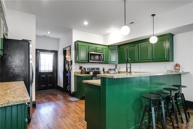 kitchen featuring kitchen peninsula, appliances with stainless steel finishes, green cabinetry, dark hardwood / wood-style floors, and hanging light fixtures