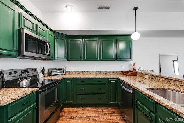 kitchen featuring dark wood-type flooring, light stone counters, pendant lighting, appliances with stainless steel finishes, and green cabinetry