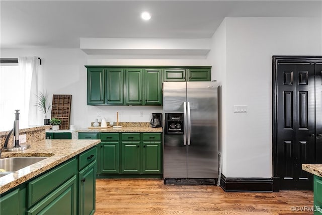 kitchen with stainless steel fridge with ice dispenser, light hardwood / wood-style floors, light stone counters, and green cabinetry