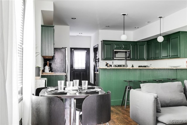 kitchen with kitchen peninsula, stainless steel appliances, dark wood-type flooring, hanging light fixtures, and green cabinets