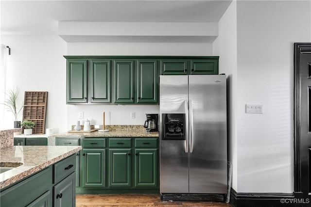 kitchen with light stone counters, hardwood / wood-style flooring, stainless steel refrigerator with ice dispenser, and green cabinetry