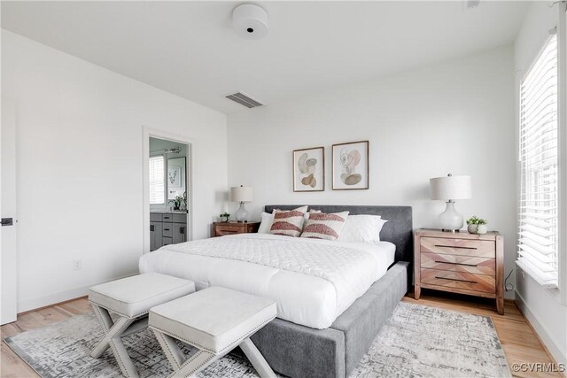 bedroom with connected bathroom, light hardwood / wood-style flooring, and multiple windows