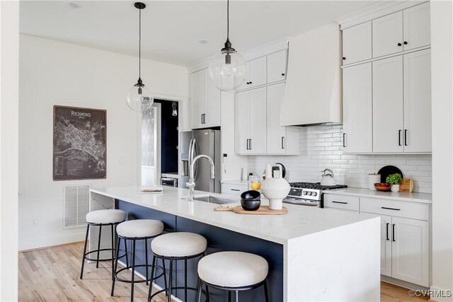 kitchen featuring white cabinets, stainless steel appliances, tasteful backsplash, and an island with sink