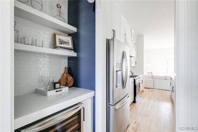 kitchen with wine cooler, decorative backsplash, light wood-type flooring, white cabinetry, and stainless steel appliances