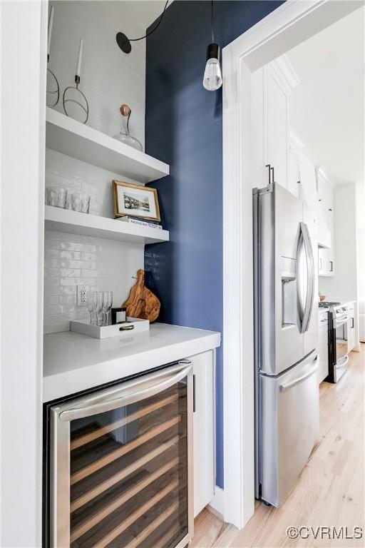 bar with stainless steel appliances, beverage cooler, decorative light fixtures, light hardwood / wood-style flooring, and white cabinets