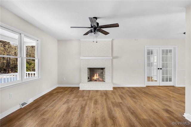 unfurnished living room featuring a brick fireplace, hardwood / wood-style floors, ceiling fan, and french doors