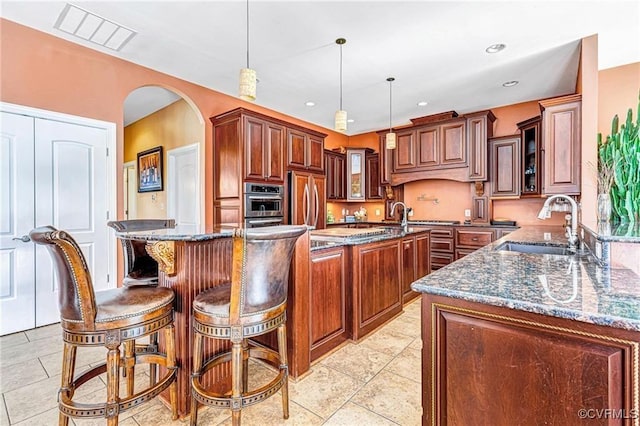 kitchen with paneled refrigerator, sink, pendant lighting, dark stone countertops, and a kitchen island