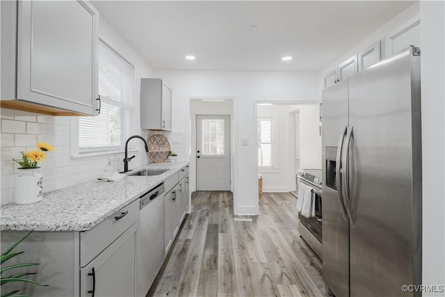 kitchen with sink, stainless steel appliances, light stone counters, plenty of natural light, and light wood-type flooring