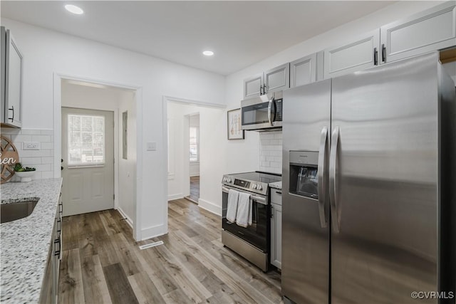 kitchen featuring light stone countertops, backsplash, stainless steel appliances, and light hardwood / wood-style flooring