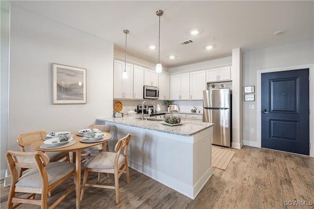 kitchen with kitchen peninsula, appliances with stainless steel finishes, light stone counters, white cabinets, and hanging light fixtures