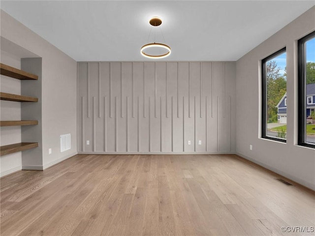 empty room with built in shelves and light wood-type flooring