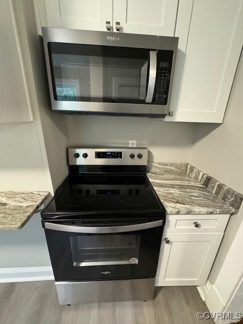 kitchen with white cabinets, light wood-type flooring, stainless steel appliances, and light stone countertops