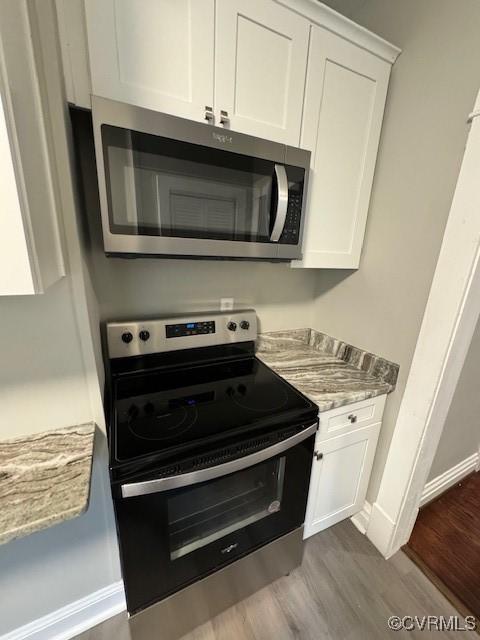 kitchen featuring white cabinets, wood-type flooring, stainless steel appliances, and light stone countertops