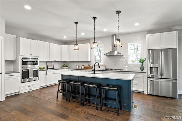 kitchen featuring white cabinets, decorative light fixtures, wall chimney range hood, and stainless steel appliances