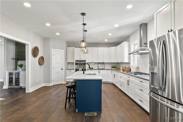 kitchen with white cabinetry, sink, wall chimney exhaust hood, stainless steel appliances, and an island with sink