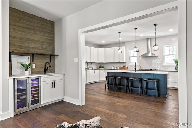 kitchen with wall chimney exhaust hood, beverage cooler, white cabinets, dark hardwood / wood-style floors, and a breakfast bar area