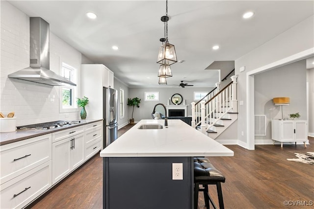 kitchen featuring sink, wall chimney exhaust hood, backsplash, a center island with sink, and appliances with stainless steel finishes