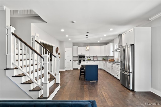 kitchen with pendant lighting, a kitchen bar, a kitchen island with sink, white cabinets, and appliances with stainless steel finishes