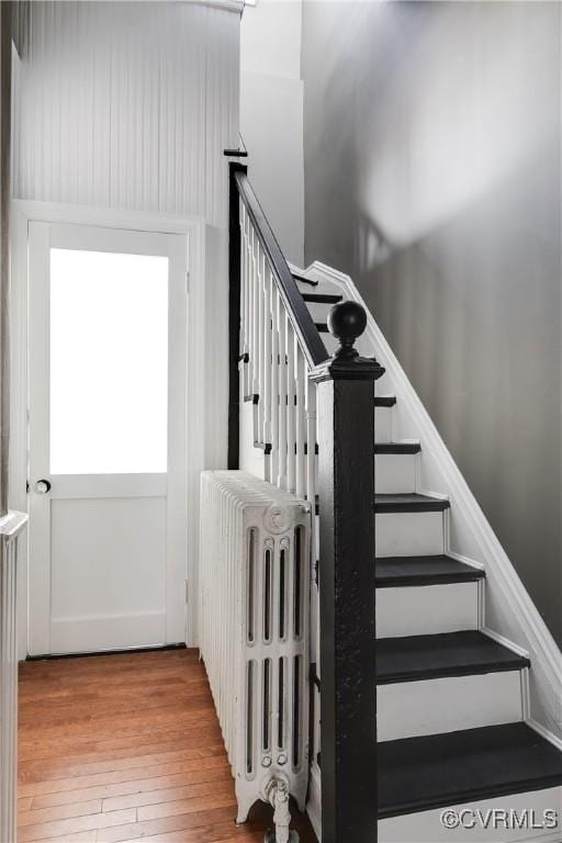 stairs with hardwood / wood-style floors and radiator heating unit