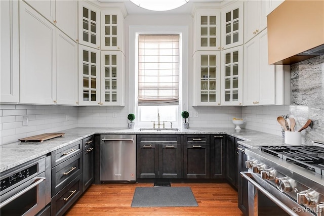 kitchen featuring appliances with stainless steel finishes, white cabinetry, sink, light stone countertops, and light wood-type flooring